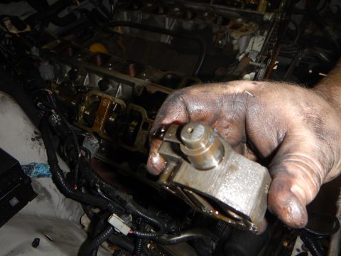 2002 Ford Mustang - Mechanic's hands work on an engine, holding a part removed from the engine block.