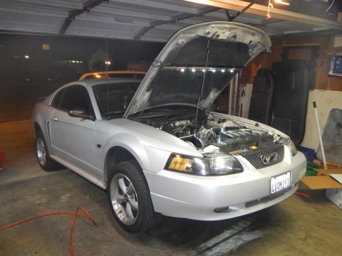 2002 Ford Mustang - The front of a silver 2002 Ford Mustang is visible with its hood open, revealing the engine compartment and auxiliary lighting.