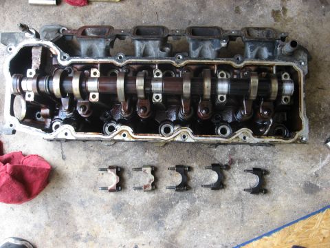 1994 Ford Bronco - Disassembled engine cylinder head with camshaft and rocker arms visible, parts laid out on a concrete surface.