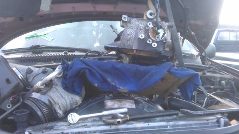1994 Ford Bronco - A vehicle's engine bay is open with a component being lifted out by a hoist, and tools are resting on the radiator.