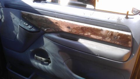 1994 Ford Bronco - Close-up of a worn interior car door panel, showing damage to the wood trim.
