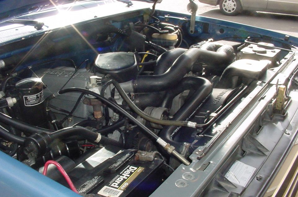 Engine bay of blue Ford Bronco with inline-six engine, black hoses, and DieHard battery