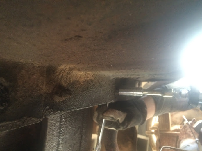 Close-up of a person's gloved hands using a socket wrench on the underbody of a vehicle
