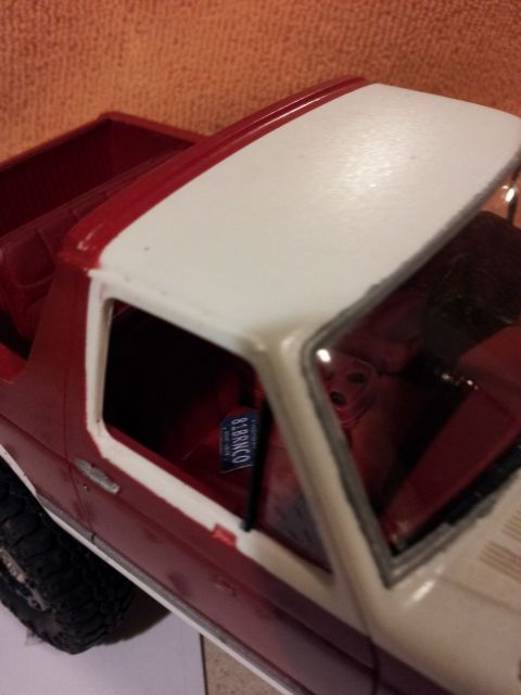 1995 Ford Bronco - A close-up view of a model car's side, showing a red body with a white roof and a small blue license plate.