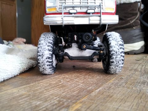 1995 Ford Bronco - A toy truck's front end is covered in snow, revealing its mechanical components and tire tread.