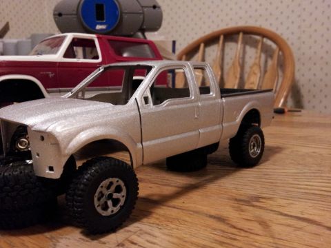 1995 Ford Bronco - Two model vehicles are on a wooden surface, with a chair and other objects in the background.