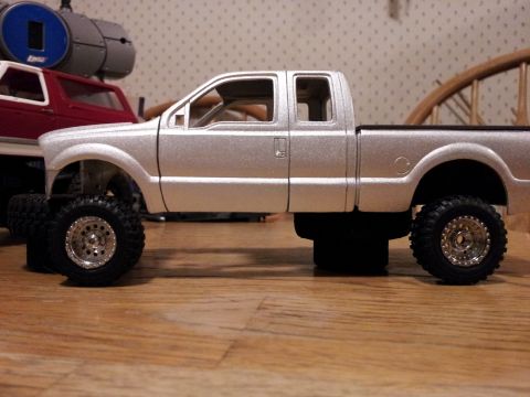 1995 Ford Bronco - A silver model pickup truck with oversized wheels is shown, with a red model truck in the background.