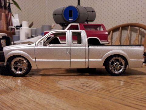 1995 Ford Bronco - A silver pickup truck model is shown with a red SUV model in its bed, against a backdrop of crafting supplies.