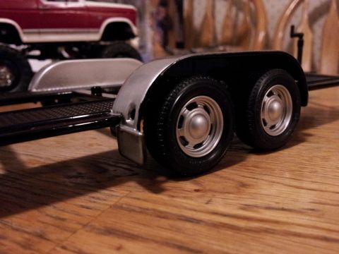 1995 Ford Bronco - Model trailer with dual wheels and a red model truck in the background on a wooden surface.