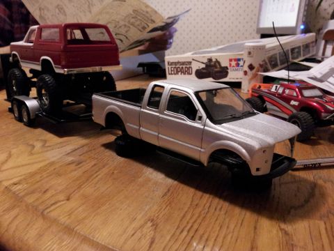 1995 Ford Bronco - Model trucks and trailer on a wooden surface with other hobby items in the background.