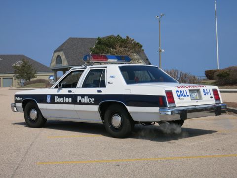 1991 Ford LTD Crown Victoria - A Boston Police car is parked in a lot, with smoke billowing from its exhaust pipe.