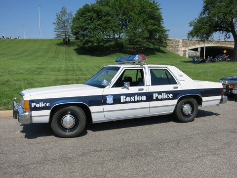 1991 Ford LTD Crown Victoria - A white and blue police car with a light bar on the roof is parked on pavement.