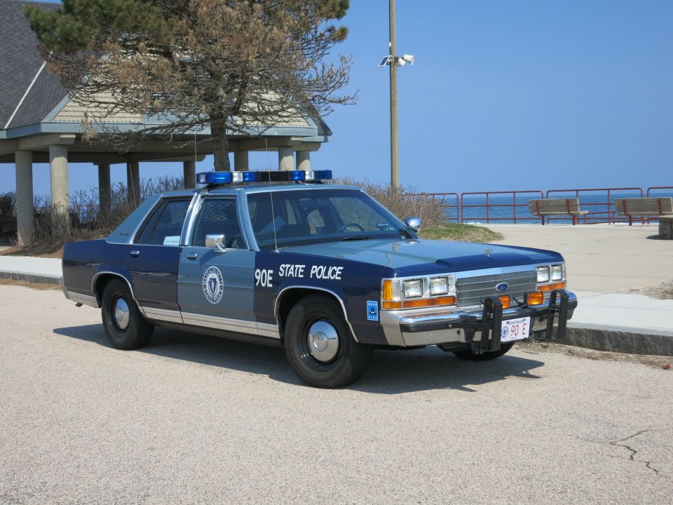 Ford police car with blue lights on roof, parked near a beach pavilion
