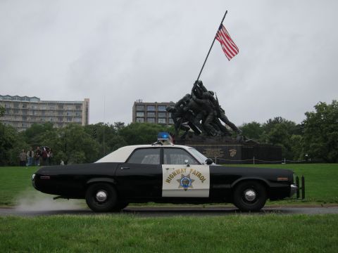 1991 Ford LTD Crown Victoria - A vintage police car drives by the Marine Corps War Memorial on a cloudy day.