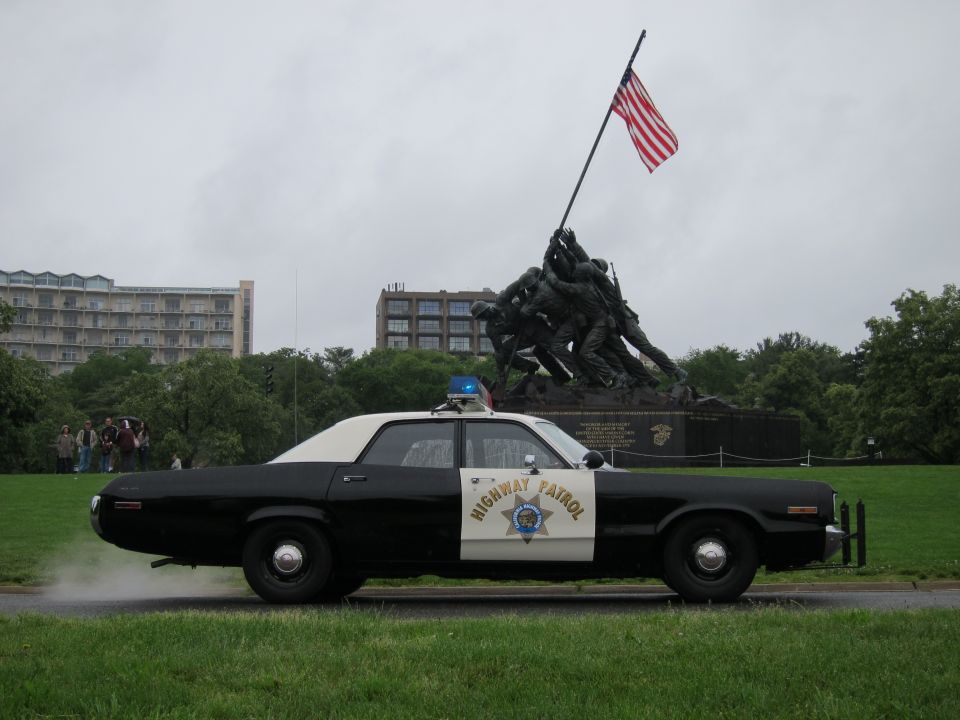 Black and white police car with "HIGHWAY PATROL" on door, side view, emitting smoke from rear