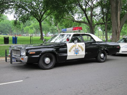1991 Ford LTD Crown Victoria - Black-and-white Dodge Polara four-door sedan in California Highway Patrol markings, parked curbside along a shaded park drive and viewed fr…