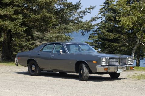 1991 Ford LTD Crown Victoria - Charcoal-gray unmarked-style late-1970s Dodge Monaco four-door sedan on gravel at a wooded lakeshore, shown from the driver-side front thre…