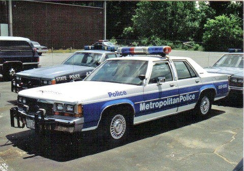 1991 Ford LTD Crown Victoria - Low-resolution photo of a white Ford LTD Crown Victoria sedan lettered 'Metropolitan Police' in blue along a blue body stripe, with a blue-…