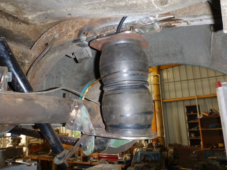 Close-up of an aftermarket air suspension bag mounted to a vehicle's rear axle assembly. Some rust is visible on the chassis