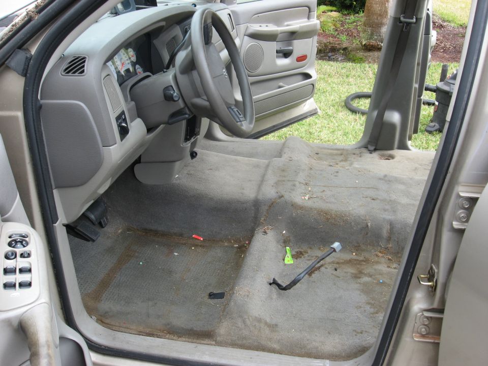 Interior of a dirty, tan Dodge Ram 1500 with the driver's door open, showing the dashboard, steering wheel, and floor