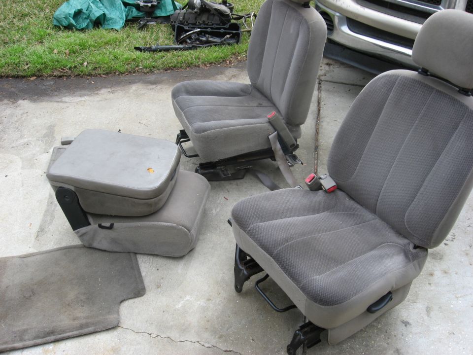 Two gray cloth vehicle seats and a gray center console with storage compartment, on concrete