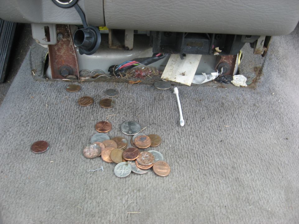 Interior floor of a vehicle with scattered coins and a q-tip