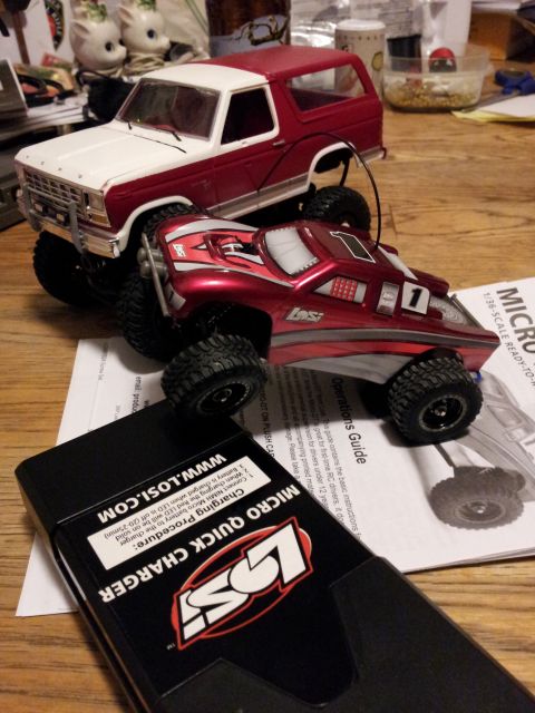 1995 Ford Bronco - Two toy vehicles, a Ford Bronco and a remote control car, sit on a wooden surface with a charger and instructions.
