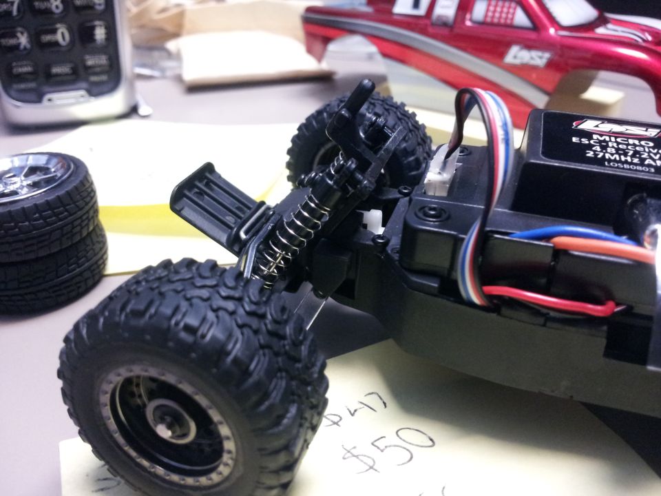 Remote control car chassis with exposed wiring and suspension components, next to stacked tires