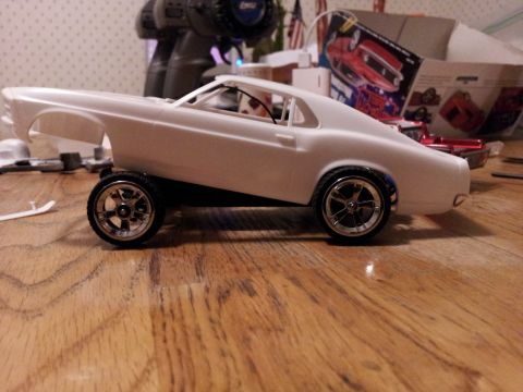 1995 Ford Bronco - A white model car body sits on a chassis with custom wheels, with hobby supplies in the background.
