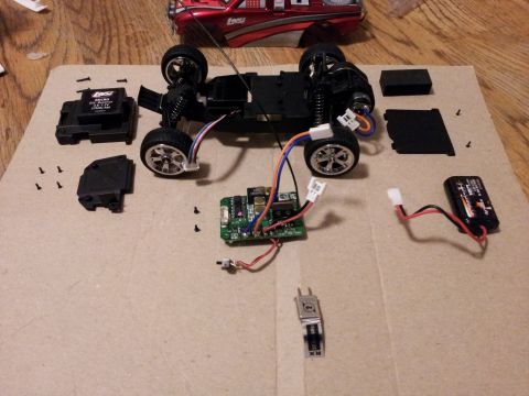 1995 Ford Bronco - Disassembled remote control car chassis and parts laid out on a cardboard surface, showing the electronic components and battery.