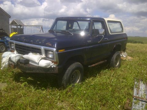 1979 Ford Bronco - This Ford Bronco is parked in a grassy field next to a building and a swing set.