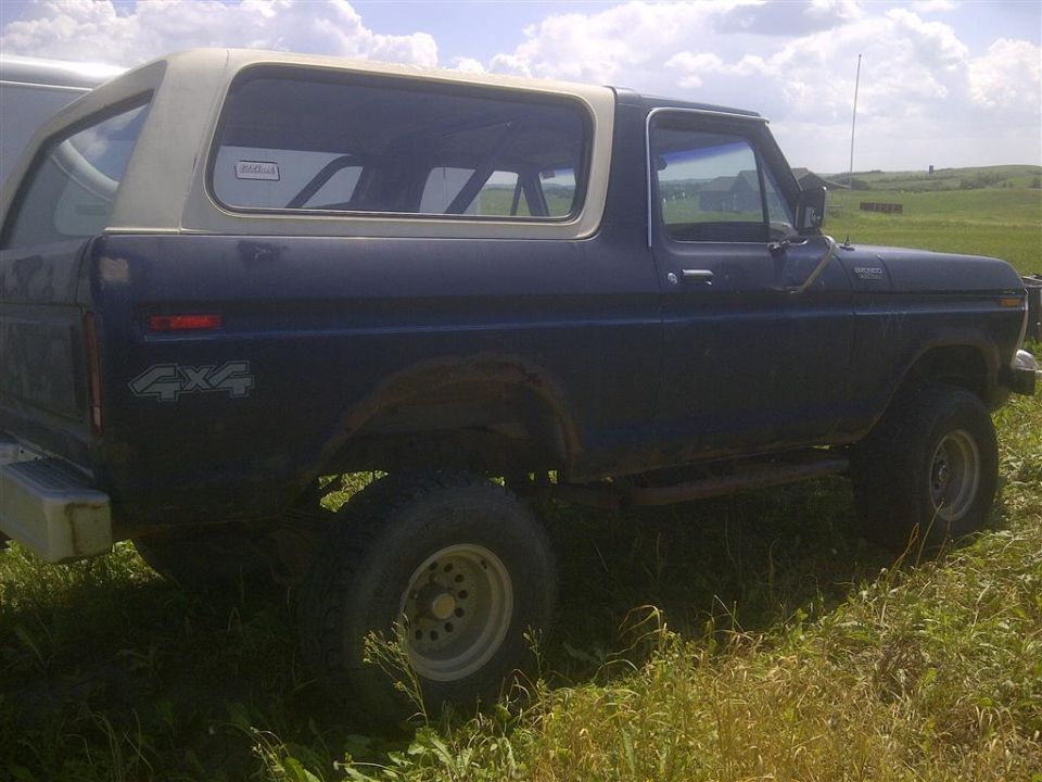 Dark blue Ford Bronco with a white top, parked in grass. Has 4x4 decal on rear fender
