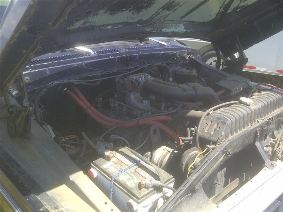 Engine bay of a 1979 Ford Bronco with the hood open, showing the V8 engine, battery, and radiator