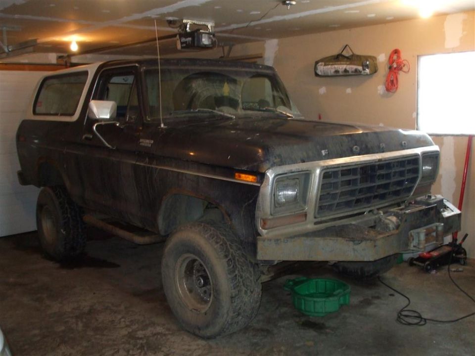 Dark Ford Bronco with white top, parked in a garage. Aftermarket bumper installed