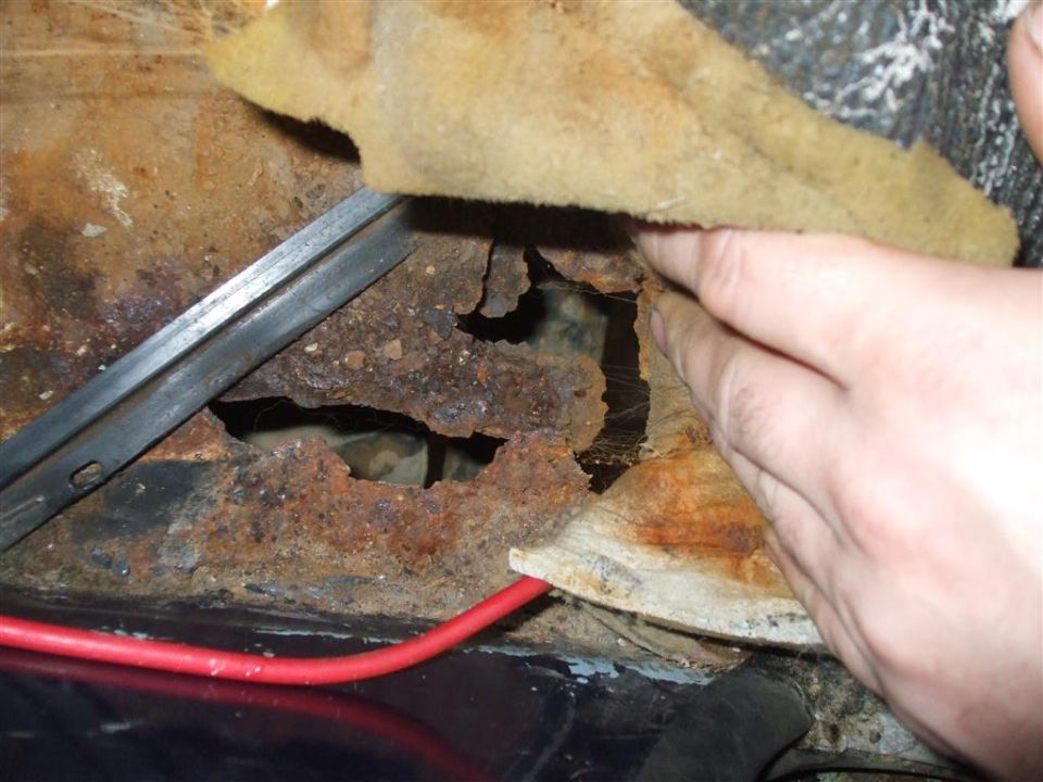 Rusted floor pan with large hole and red wire