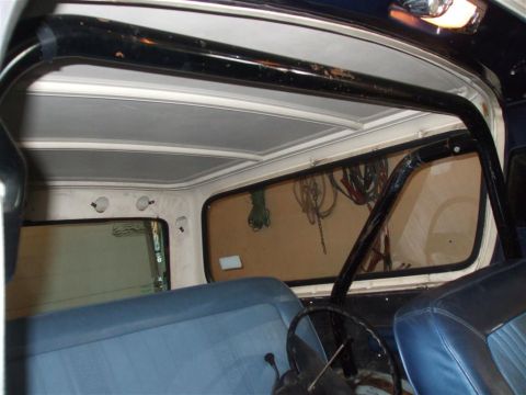 1979 Ford Bronco - The interior of a vehicle shows a roll cage and blue upholstered seats, with a view through the rear window.
