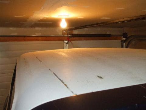 1979 Ford Bronco - The roof of a white vehicle is visible inside a garage, illuminated by a bare light bulb.
