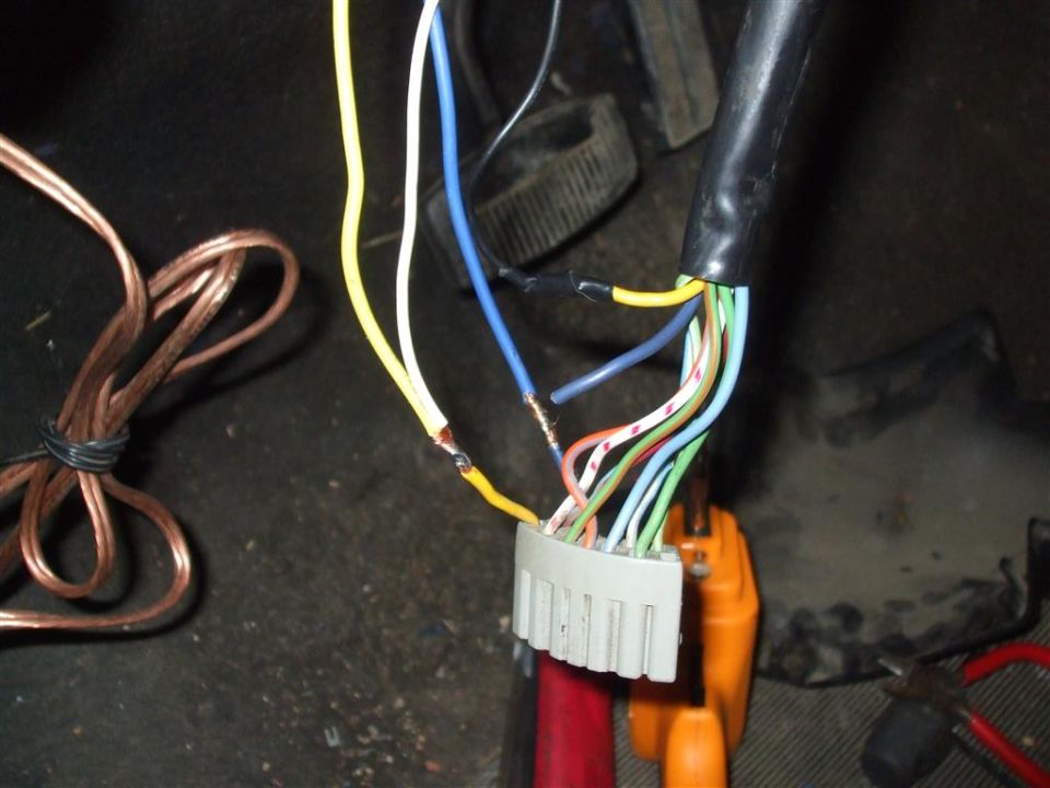 Close-up of a vehicle's wiring harness with multiple colored wires connected to a white connector. Some wires are exposed and twisted