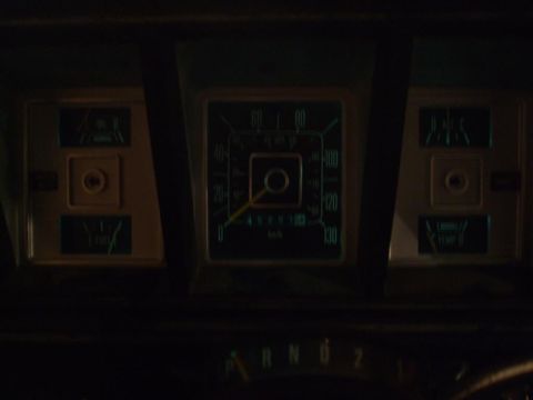 1979 Ford Bronco - A close-up view of a vehicle's dashboard gauges and gear selector, illuminated in the dark.
