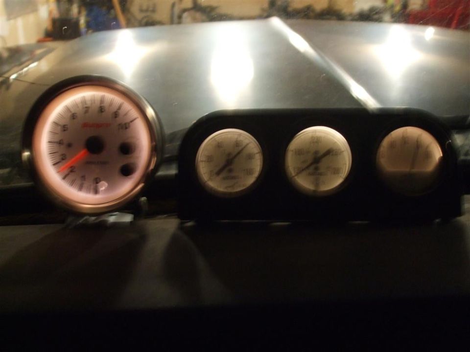 Gauges lit up on a dashboard, one is a tachometer, others are smaller gauges
