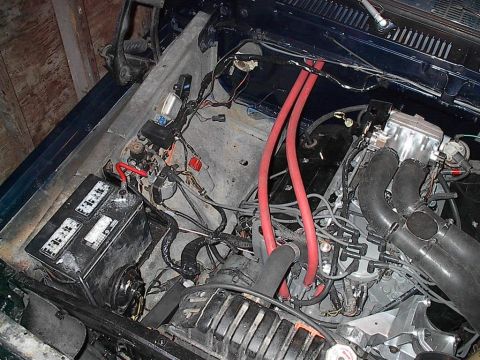 1979 Ford Bronco - The engine bay of a vehicle, a battery, wiring, and engine parts, with a watermark for SuperMotors.net.