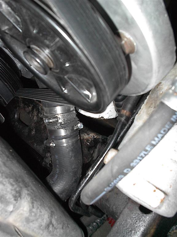 Close-up of a car's engine bay showing a ribbed belt on a pulley and a black hose with metal clamps