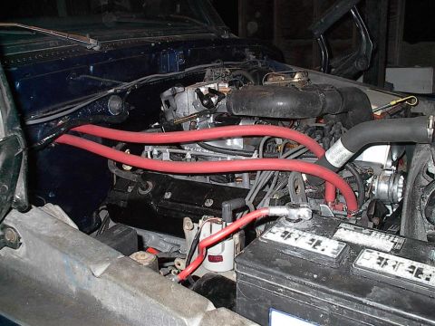 1979 Ford Bronco - Close-up of an engine bay with prominent red spark plug wires and battery.