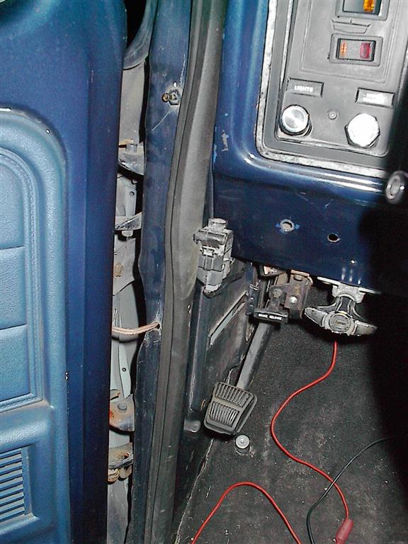 Close-up of a blue car's interior door jamb and part of the dashboard, showing pedals and wiring