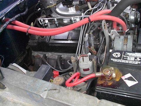 1979 Ford Bronco - The engine bay shows a battery with corroded terminals and various hoses and wires connected to the engine block.