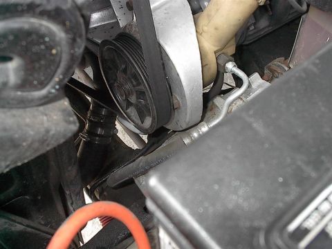 1979 Ford Bronco - Engine compartment detail showing a belt driving a pulley, with various hoses and metal parts visible.