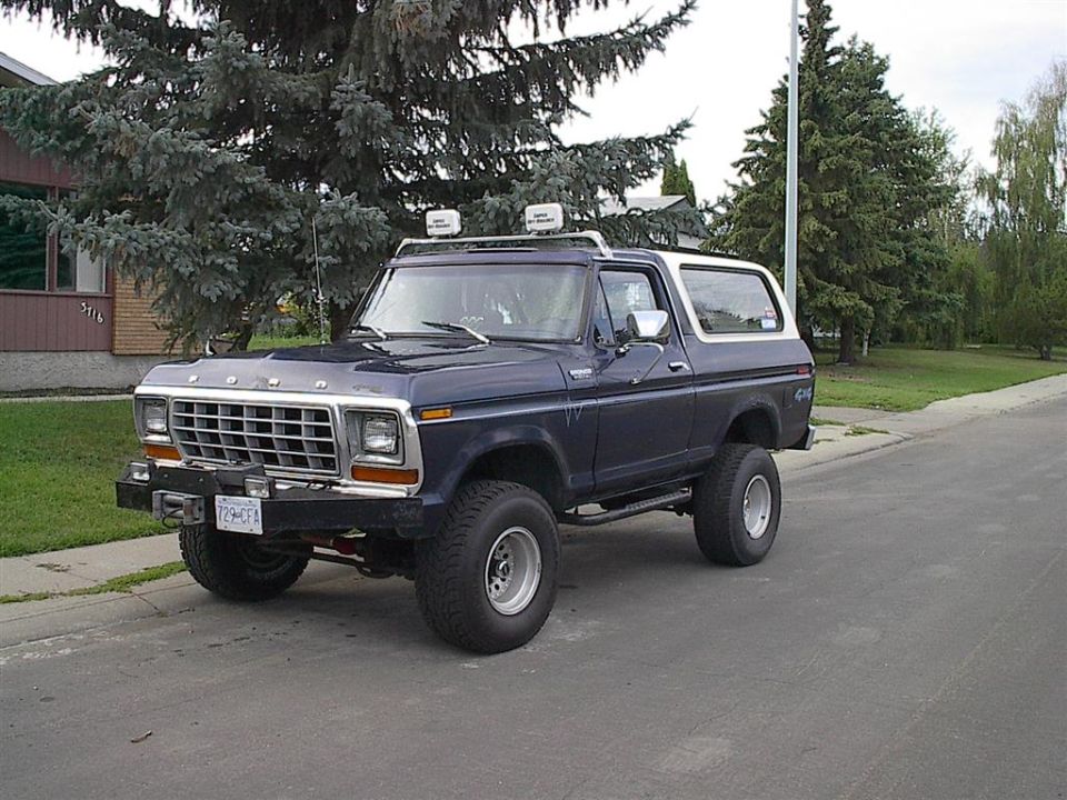 Dark blue Ford Bronco with white top, off-road tires, and roof lights parked on a street. License plate reads 729-CFA