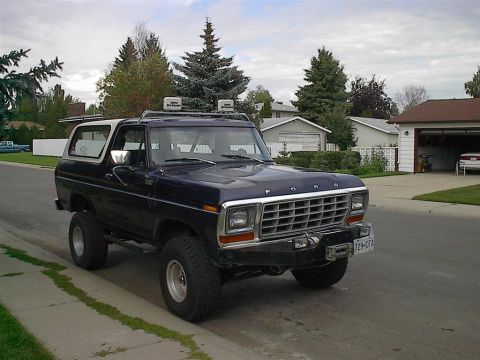 1979 Ford Bronco - This 1979 Ford Bronco, seen from a three-quarter front view, is parked on a residential street with a white top and off-road tires.