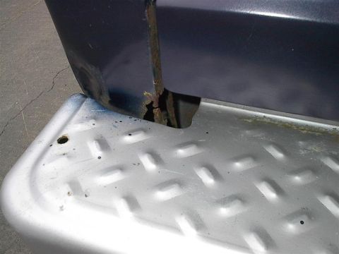 1979 Ford Bronco - The rear corner of a dark blue vehicle shows rust and damage near a silver diamond plate step.
