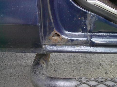 1979 Ford Bronco - Close-up of a blue vehicle's door sill showing rust damage and a portion of a running board.
